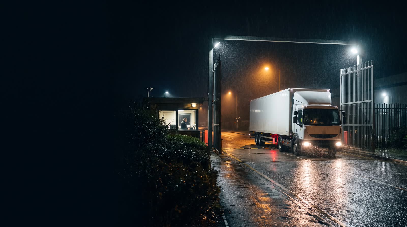 An articulated lorry pulling out of a distribution centre gate at night
